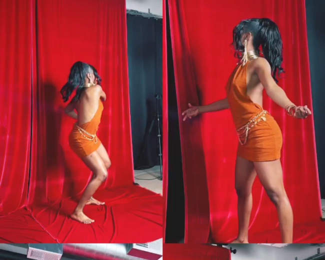 The image shows a woman in an orange dress dancing in front of a red curtain, while a person with a camera captures the moment.