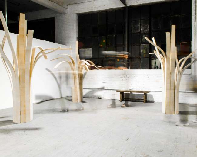 The image shows a spacious interior featuring three large wooden sculptures that resemble abstract trees, with a bench positioned in front of them.