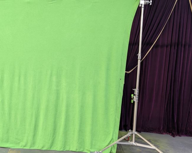 A green screen setup on a metal frame in front of a dark curtain backdrop.