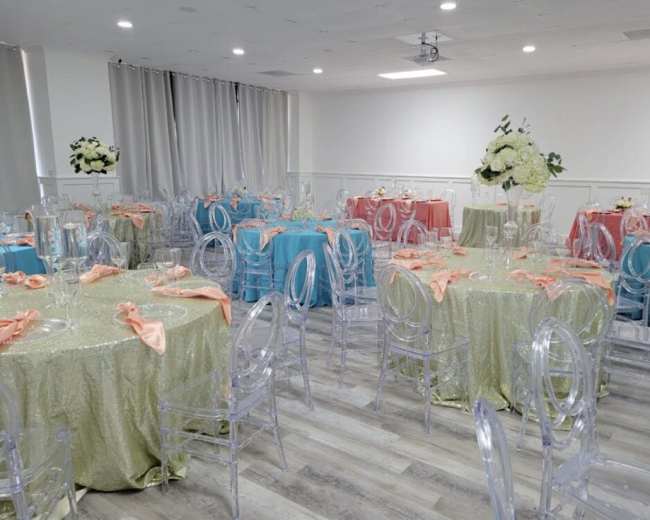 A banquet hall set up with tables covered in various colored tablecloths and clear plastic chairs, ready for an event.
