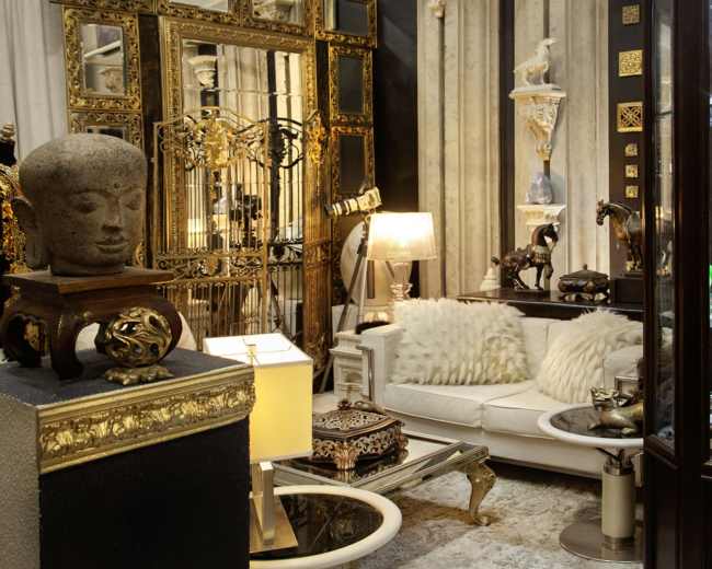 The scene depicts an elegantly decorated room featuring a white couch, various decorative artifacts, a large ornate mirror, and a display cabinet showcasing intricate items.