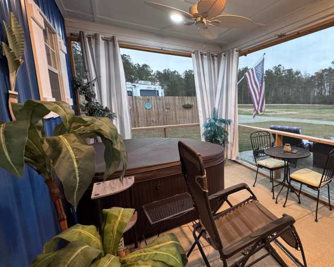 A screened porch features a hot tub, a small table with chairs, and an American flag visible outside through the open window.