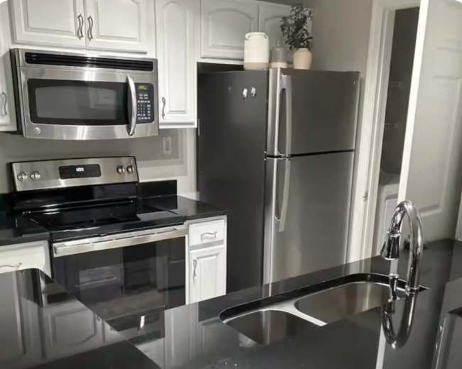 The image shows a modern kitchen with stainless steel appliances, white cabinetry, and a dark countertop featuring a sink.
