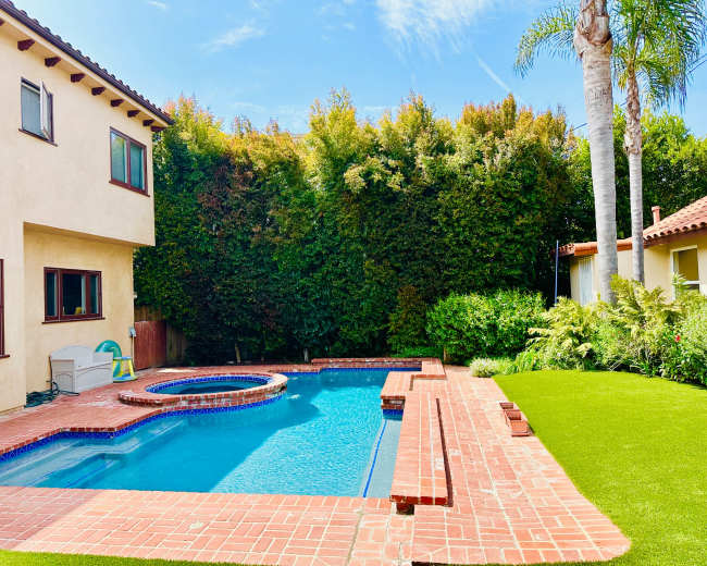 A swimming pool with a spa and patio area is surrounded by lush greenery and a well-maintained lawn.