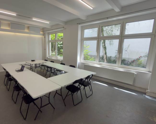 A bright meeting room features a large central table surrounded by black chairs and large windows allowing natural light to enter.