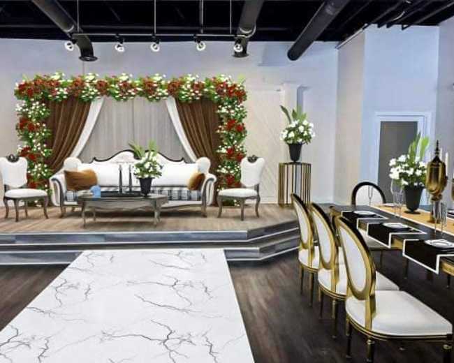 The scene features an elegantly decorated event space with a floral backdrop, a sofa, a coffee table, and a dining area set with chairs and a contrasting table.