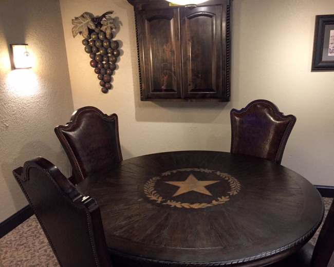 A round wooden dining table with a star and laurel design is accompanied by four dark leather chairs in a cozy, softly lit room.