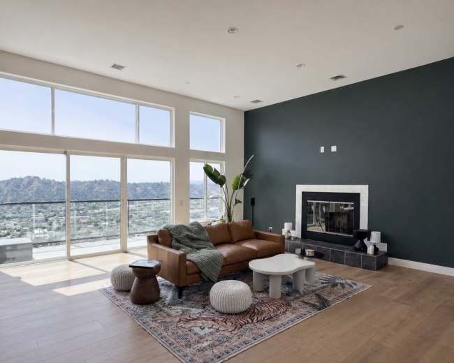 The image shows a modern living room with a brown leather sofa, a white coffee table, a fireplace, and large windows overlooking a mountain view.