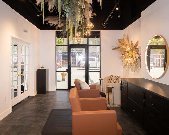 A modern interior space featuring brown leather seating, a dark cabinet, and decorative wall elements, with large windows allowing natural light to enter.