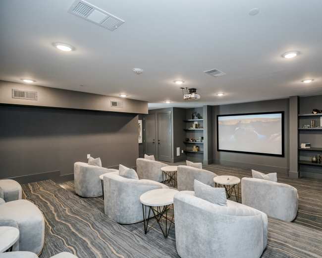 The image shows a modern home theater with plush seating arranged in rows facing a large projection screen on one wall.