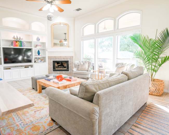The living room features a white entertainment center, a light-colored sofa, a coffee table, and large windows providing ample natural light.