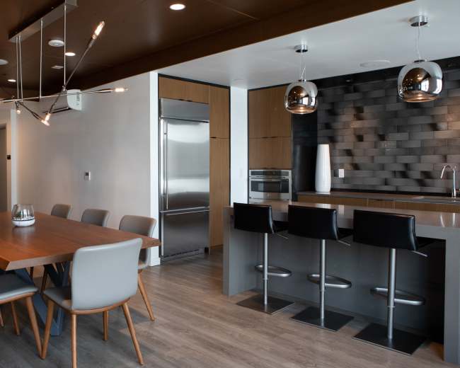 A modern kitchen and dining area featuring a wooden dining table with eight chairs, a sleek kitchen island with bar seating, and stainless steel appliances.