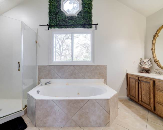 The bathroom features a corner jetted bathtub, a glass-enclosed shower, and a wooden vanity with a round mirror.