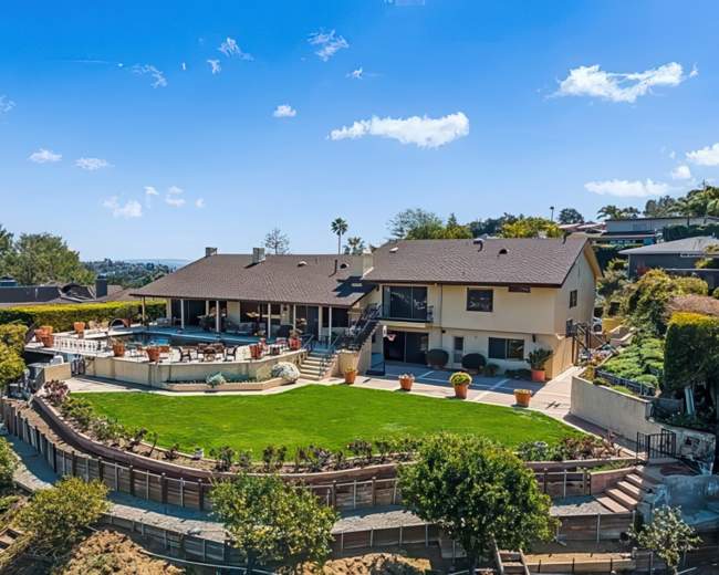 A hillside home features a large backyard with a swimming pool, surrounded by landscaped greenery and outdoor seating areas.