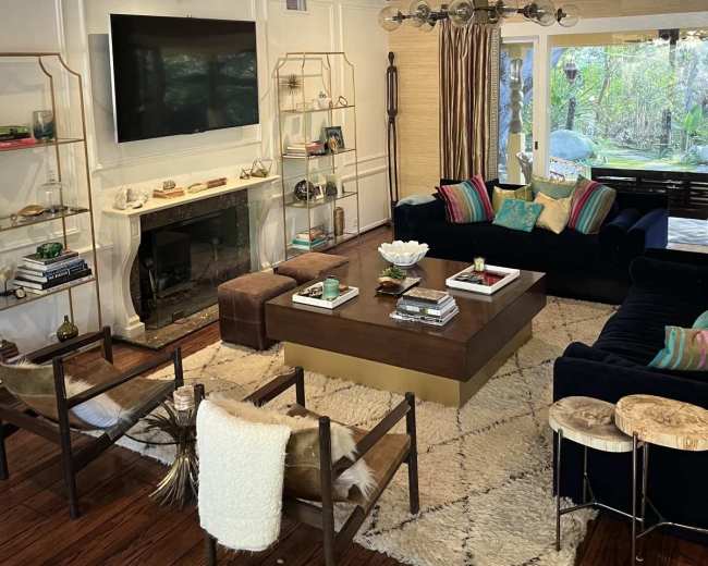 The living room features a dark blue sectional sofa, a wooden coffee table, a mounted television, and bookshelves displaying decorative items and books.