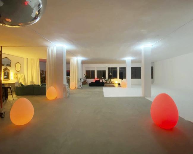A spacious room features large, glowing egg-shaped lights arranged on the floor, with white walls and large windows allowing natural light to enter.