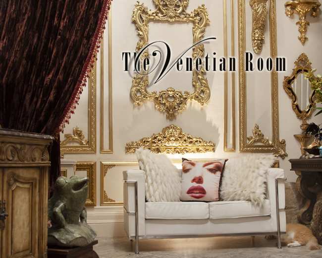 A lavishly decorated room features ornate gold wall decor, a plush white sofa, and rich burgundy drapes.