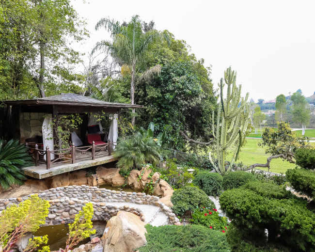 A landscaped garden features a gazebo surrounded by lush greenery, cacti, and a small pond.