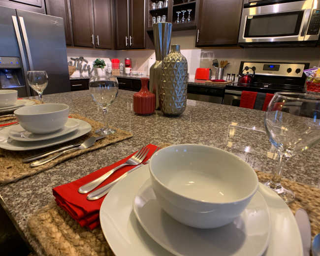 A modern kitchen countertop set for a meal, featuring polished dinnerware, glassware, and decorative elements.