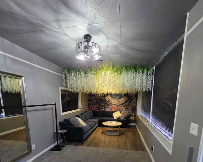 The image shows a living room with a blue couch, a circular coffee table, and a wall adorned with greenery and a mural.