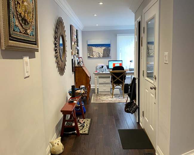 A hallway leads to a home office, featuring wooden flooring, a desk, and decorative items along the walls.