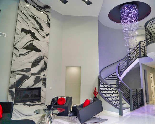 The image shows a modern living space featuring a spiral staircase, a marble accent wall, and a contemporary chandelier.