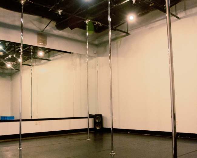 A vacant dance studio with several polished metal poles and mirrored walls.