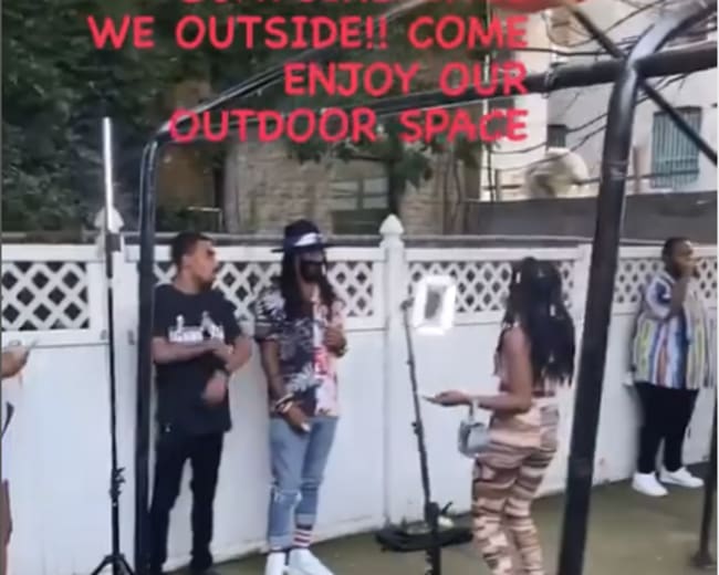 A group of people gather in an outdoor space for an event, with one person speaking on a stage-like platform.