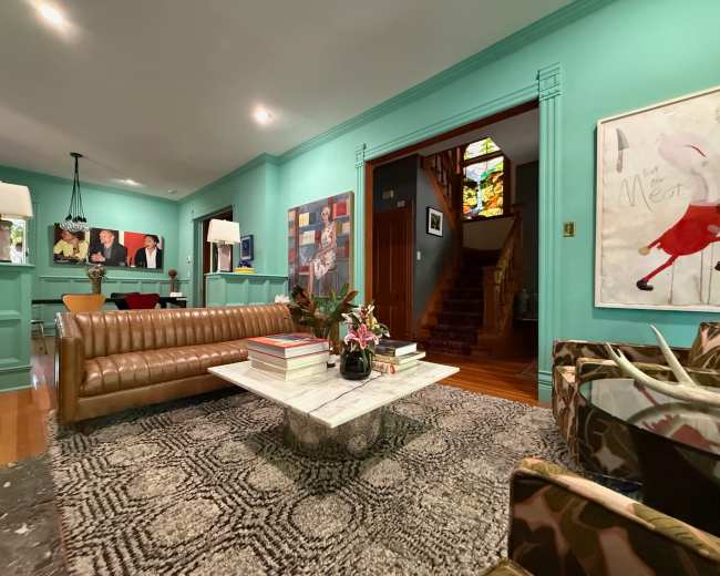 The image shows a brightly colored living room featuring a brown leather sofa, a marble coffee table, and colorful artwork on the walls.