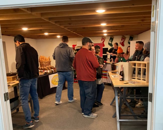 A group of people is browsing various handmade crafts and products in a spacious room decorated for a holiday event.