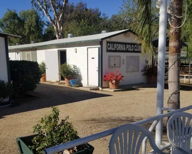 The image shows a building labeled "California Polo Club" surrounded by potted plants and a gravel pathway.