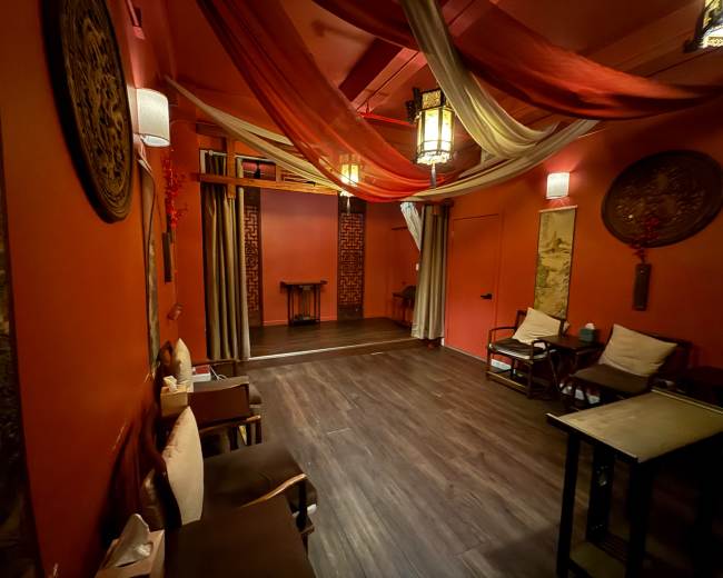 The image shows a warmly colored room with decorative drapes, wooden furniture, and art on the walls, creating a cozy atmosphere.