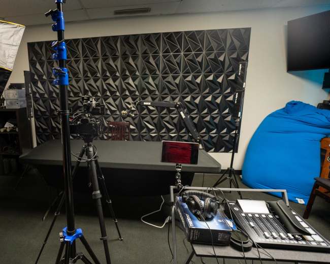 A recording studio equipped with lighting, cameras, and audio equipment, featuring a geometric soundproof wall and a large table.