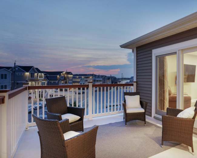 A balcony with four wicker chairs overlooks a marina at sunset.