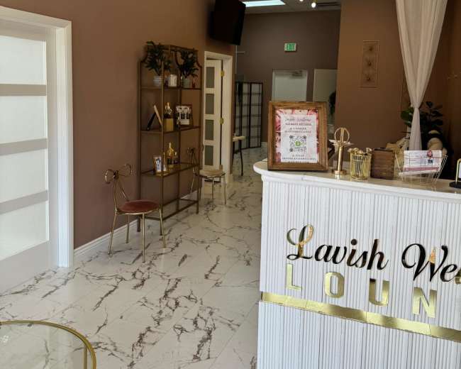 The image shows an interior of a salon or spa with a reception desk, decorative plants, and modern lighting fixtures.