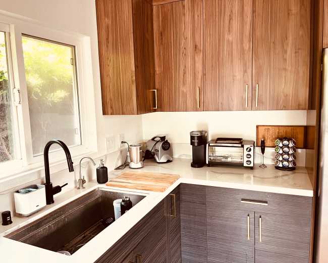 The image features a modern kitchen with wooden cabinets, a stainless steel sink, and various appliances including a coffee maker and a toaster.