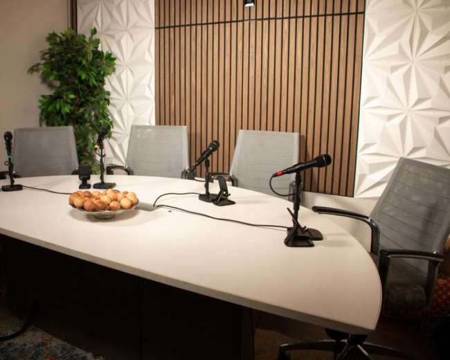 A modern conference room features a large white table with a bowl of eggs in the center, surrounded by high-backed chairs and positioned microphones.