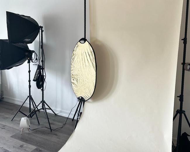 A photography studio setup with a white backdrop, softbox lights, and a reflector on stands.