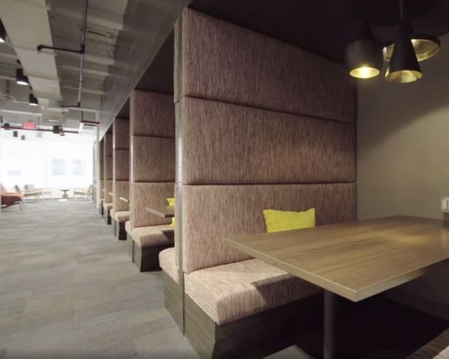 The image shows a modern, semi-enclosed seating area with upholstered booths and a wooden table under pendant lighting.