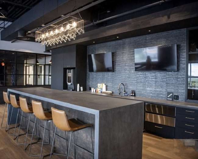The image shows a modern kitchen with a large gray island, bar stools, and two mounted flat-screen TVs on the wall.