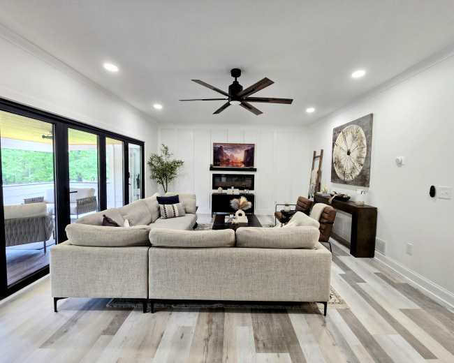 A spacious living room features a large sectional sofa, a coffee table, a wall-mounted television, and sliding glass doors leading to an outdoor space.