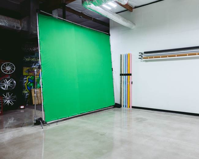 A studio space with a green screen on the left and a wall-mounted rack with rolls of colored paper on the right.