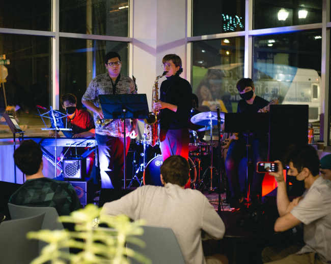 A small jazz band performs in a brightly lit café while an audience listens attentively.