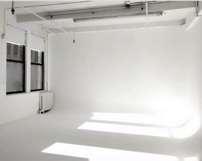 A spacious, bright room with white walls and large windows casting shadows on the floor.