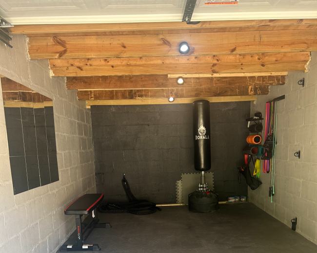A well-organized home gym with fitness equipment including a bench, a punching bag, resistance bands, and a stability ball on a rubber floor.