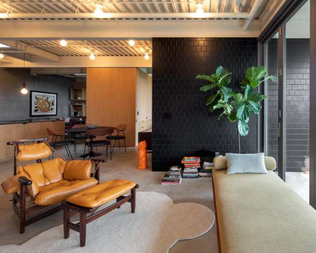 The interior of a modern living room features a yellow leather chair and a light green couch, complemented by a dark tiled wall and large windows that open to a balcony.