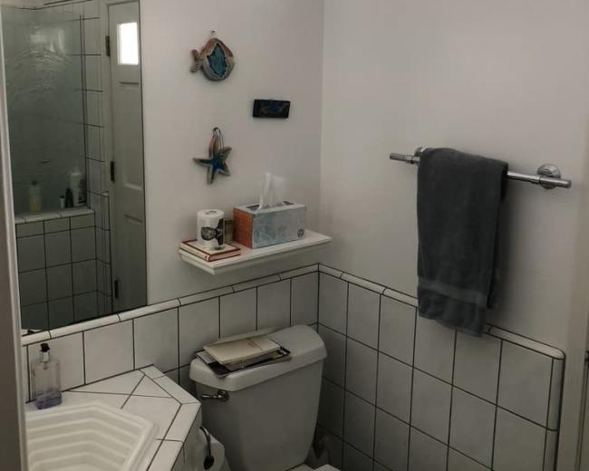The image shows a compact bathroom featuring a toilet, a sink with an octagonal shape, a mirror, and light-colored walls, along with decorative items on the wall.