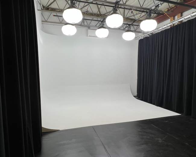 A photography studio with a seamless white backdrop, black curtains, and overhead lighting.