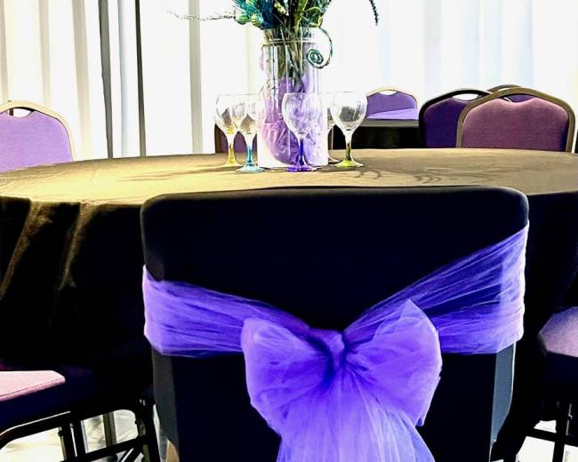 A table set with a black tablecloth and purple chairs, adorned with a tall floral centerpiece and glasses arranged neatly on the table.