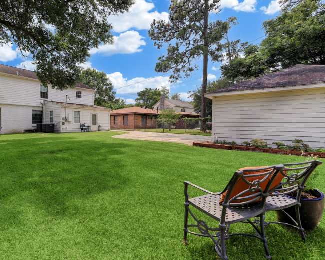 A spacious backyard featuring a well-maintained lawn, two houses, a stone patio, and outdoor seating.